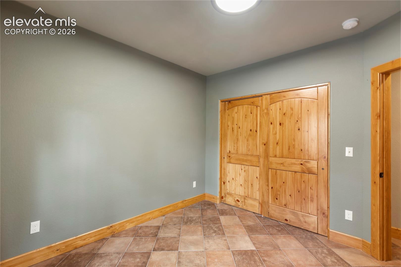 Room featuring natural wood-finish door with arched detailing, tile flooring, and matching wood trim