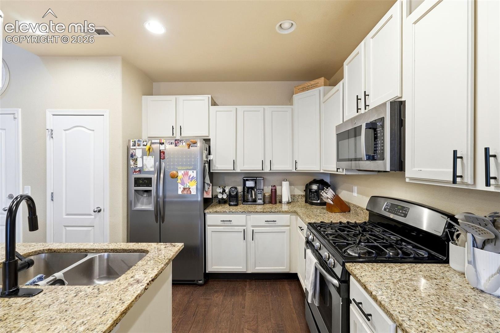 Kitchen featuring white cabinetry, stainless steel appliances, speckled countertops, a double basin sink, and wood-finish flooring