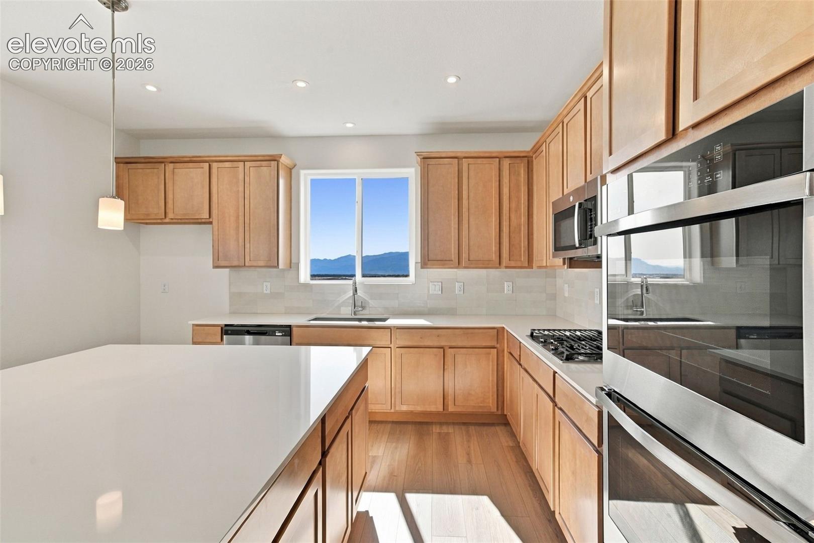 Kitchen featuring light wood cabinetry, white countertops, stainless steel appliances, and wood-finish flooring
