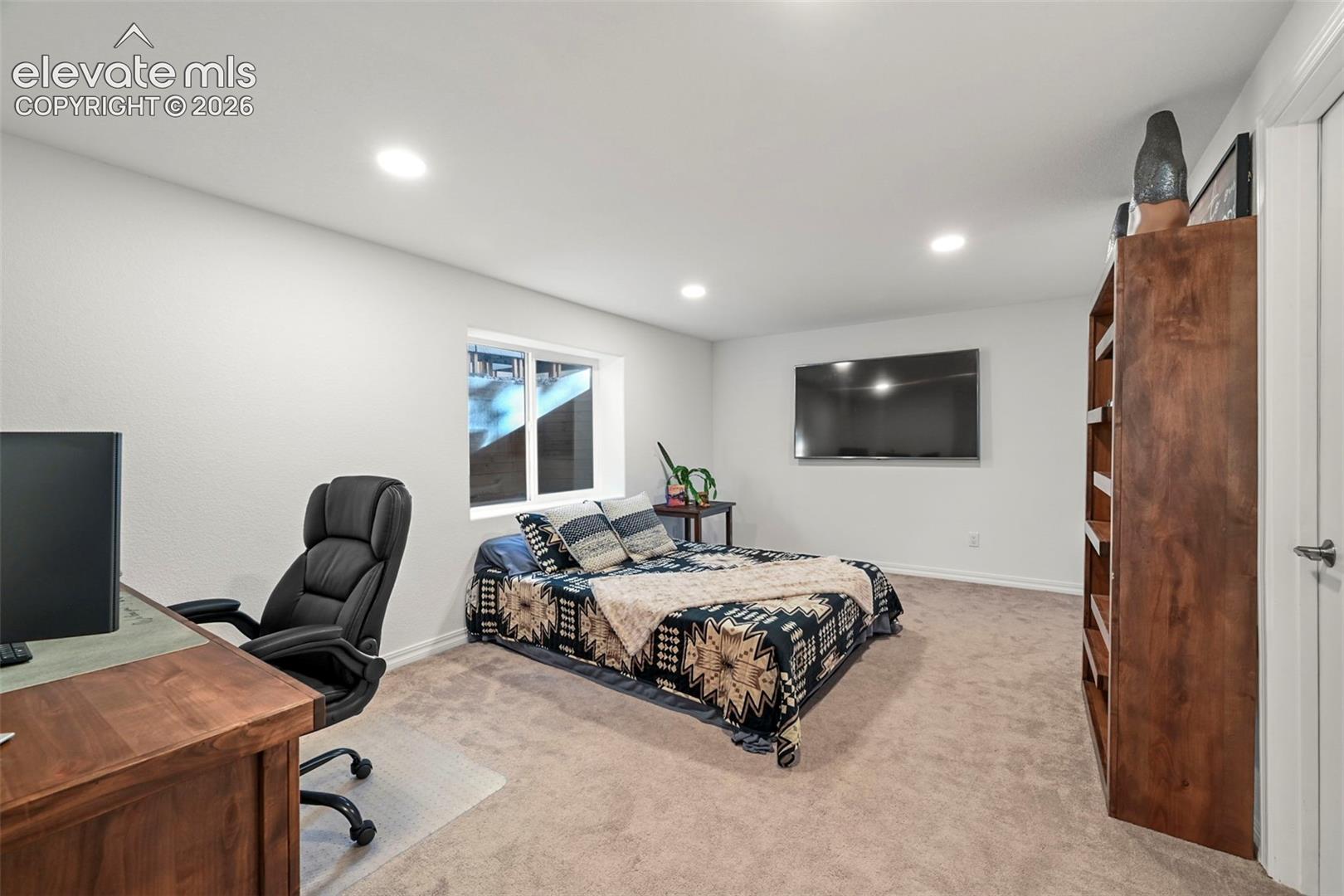 Recessed lighting, wood-finish desk, built-in shelving, carpeted flooring, and a single window