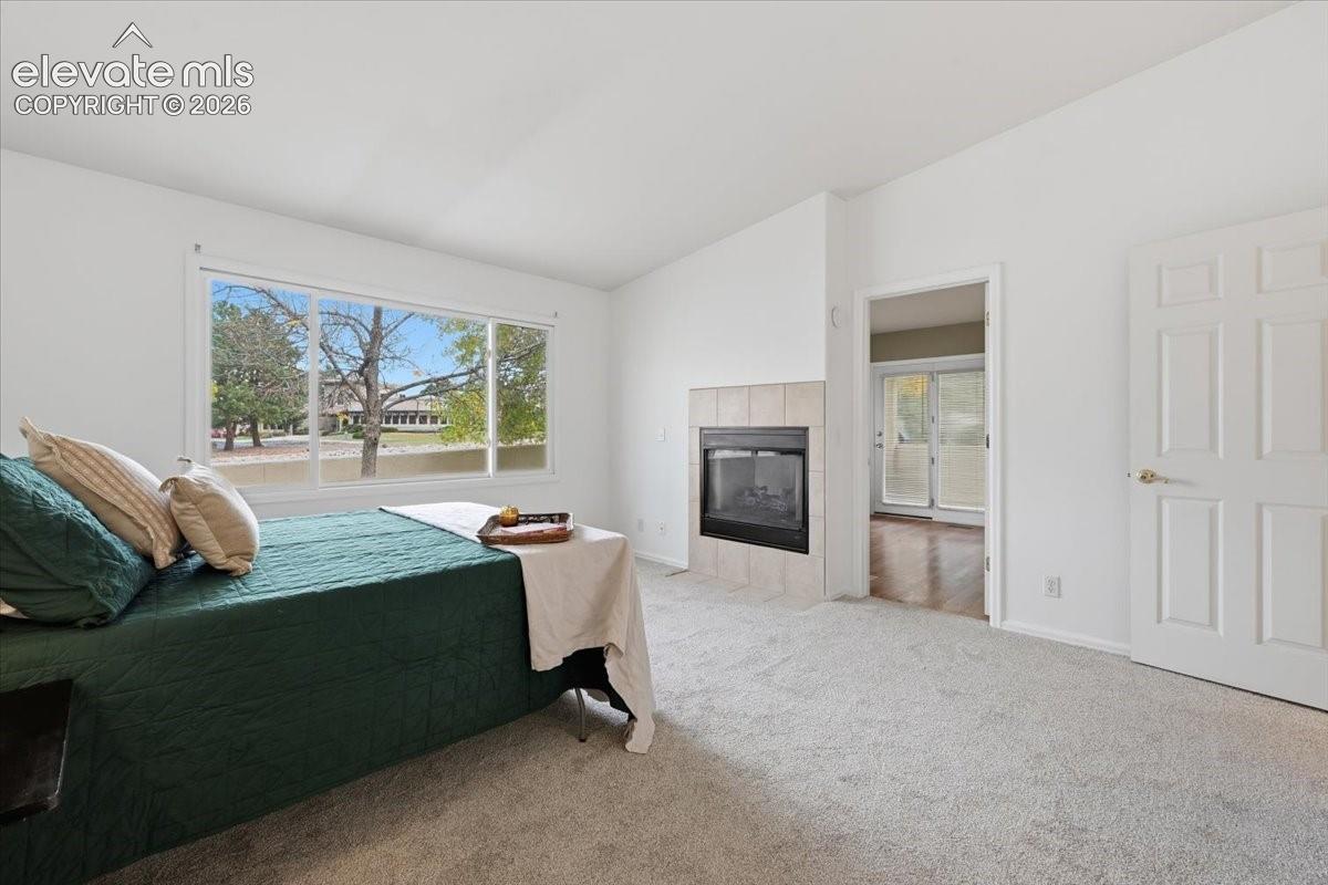 Spacious room featuring neutral carpeting, a built-in fireplace with tile surround, a large picture window, and a six-panel interior door