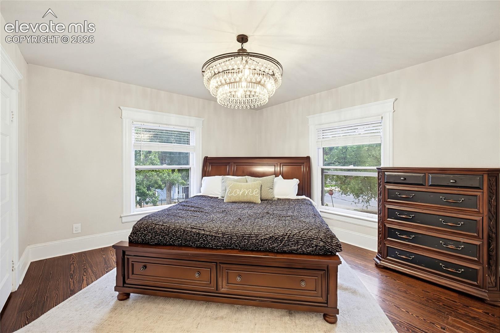 Ornate chandelier, dark wood-finish flooring, white trim windows, and light-toned walls