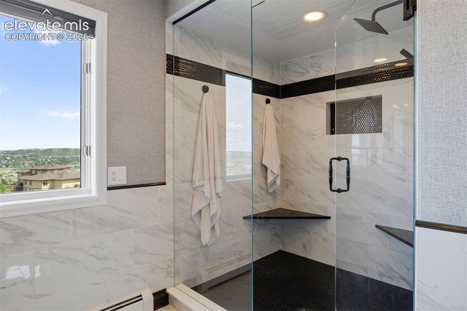 Spa-worthy walk-in shower with floor-to-ceiling marble tile, black tile floor, rain shower head, corner bench, and views.