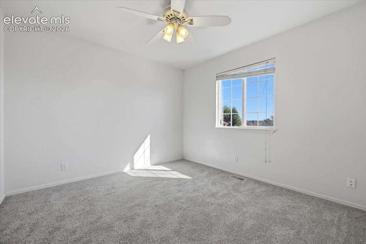 Gray carpeting, light-colored walls, window with horizontal blinds, and a ceiling fan with integrated lighting