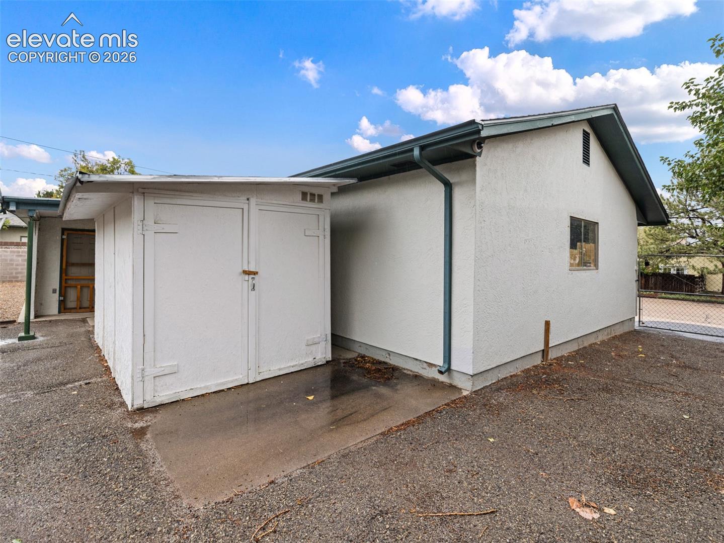 Exterior featuring stucco finish, gabled roof, and a built-in storage shed, double gate.