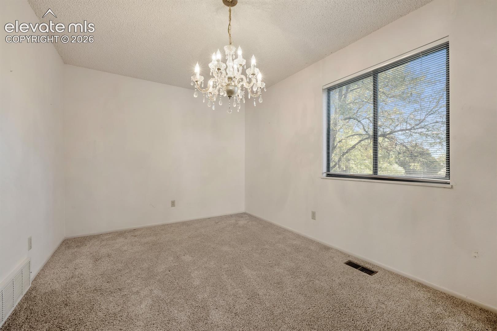 Room featuring neutral carpeting, a multi-tiered crystal chandelier, and a large window