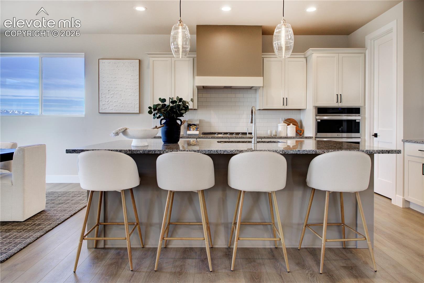 Kitchen featuring a large central island with a stone countertop, white shaker-style cabinetry, stainless steel appliances, and wood-finish flooring