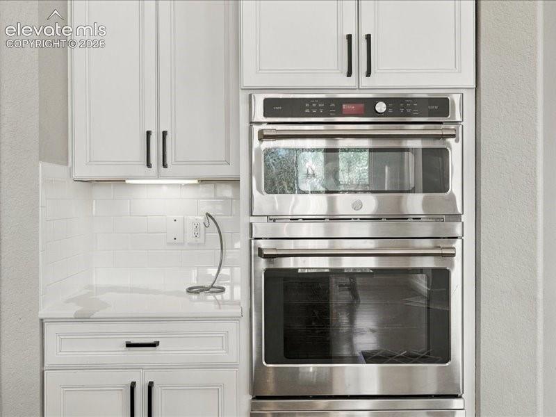 Modern kitchen featuring stainless steel double wall ovens with convection technology, white shaker-style cabinetry with brushed black hardware, white subway tile backsplash, and a quartz countertop with integrated sink and chrome faucet