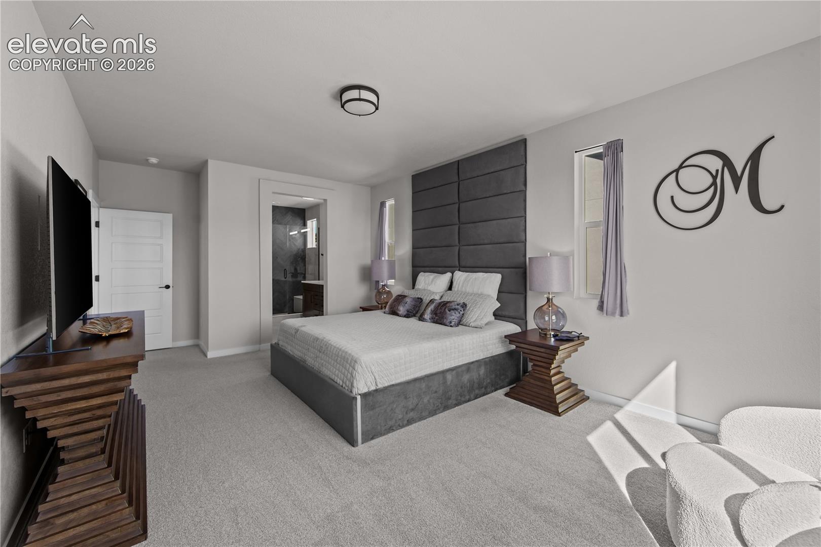 Bedroom featuring neutral wall-to-wall carpeting, flush-mount ceiling lighting, and a floor-to-ceiling upholstered wall panel accent