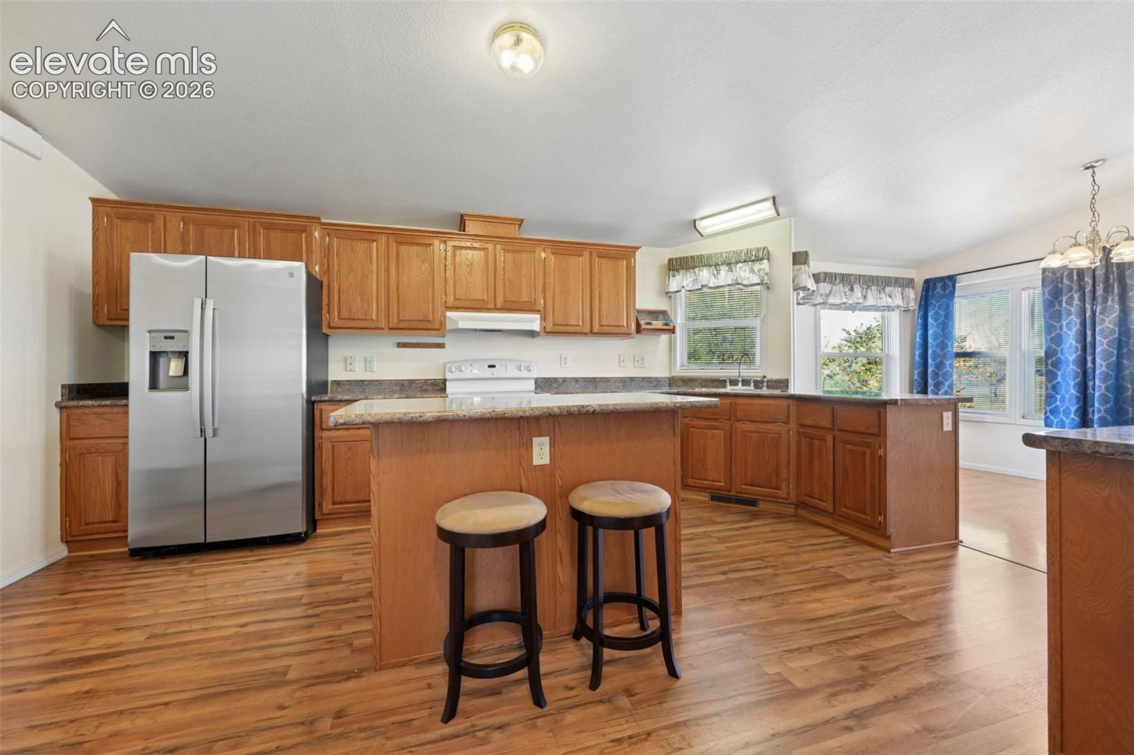 Kitchen featuring wood-finish cabinetry, stone-surfaced countertops, a center island with breakfast bar seating, stainless steel side-by-side refrigerator, and wood-finish flooring