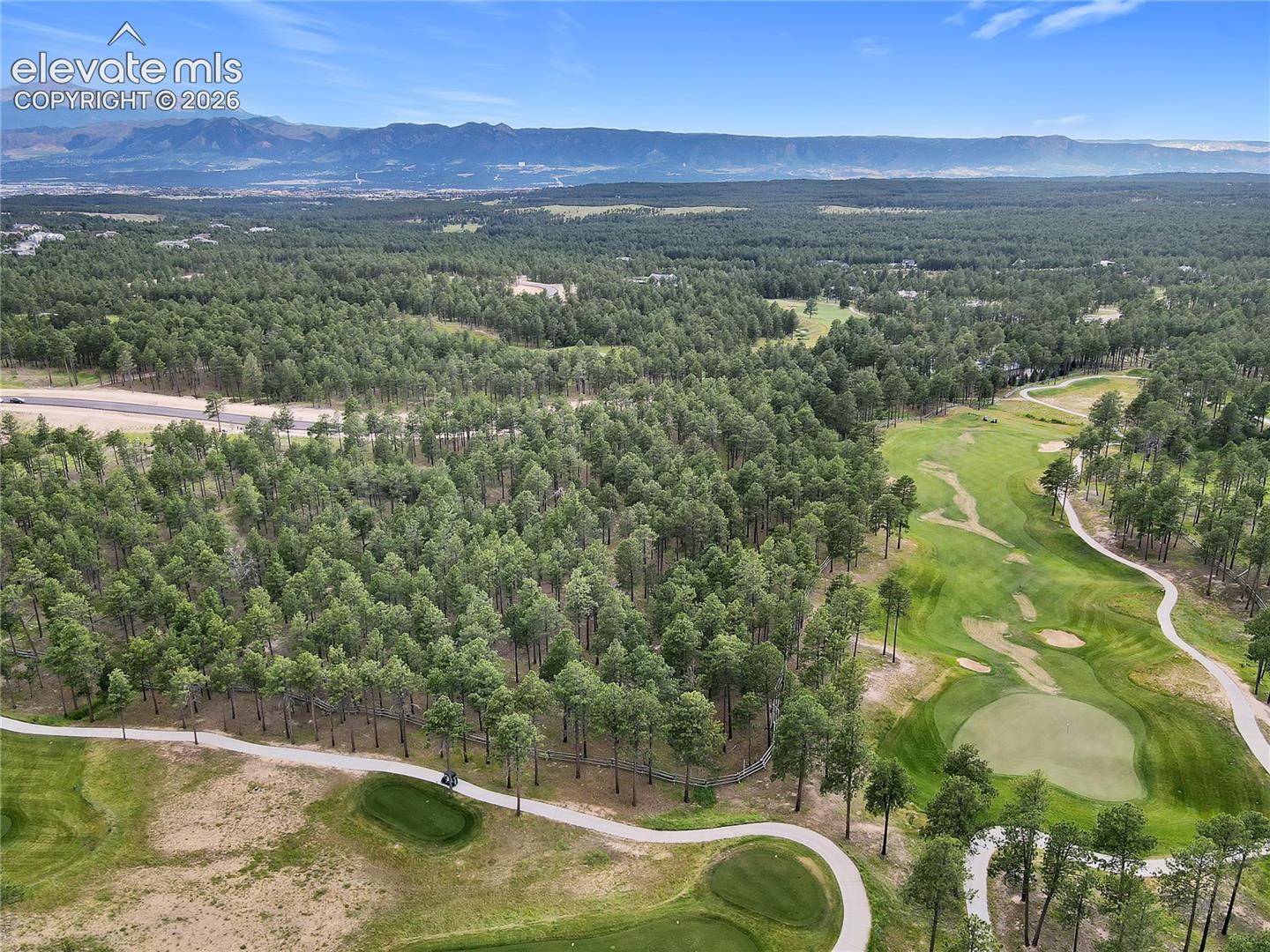Expansive lot featuring mature evergreen trees, manicured turf, winding cart paths, and distant mountain scenery