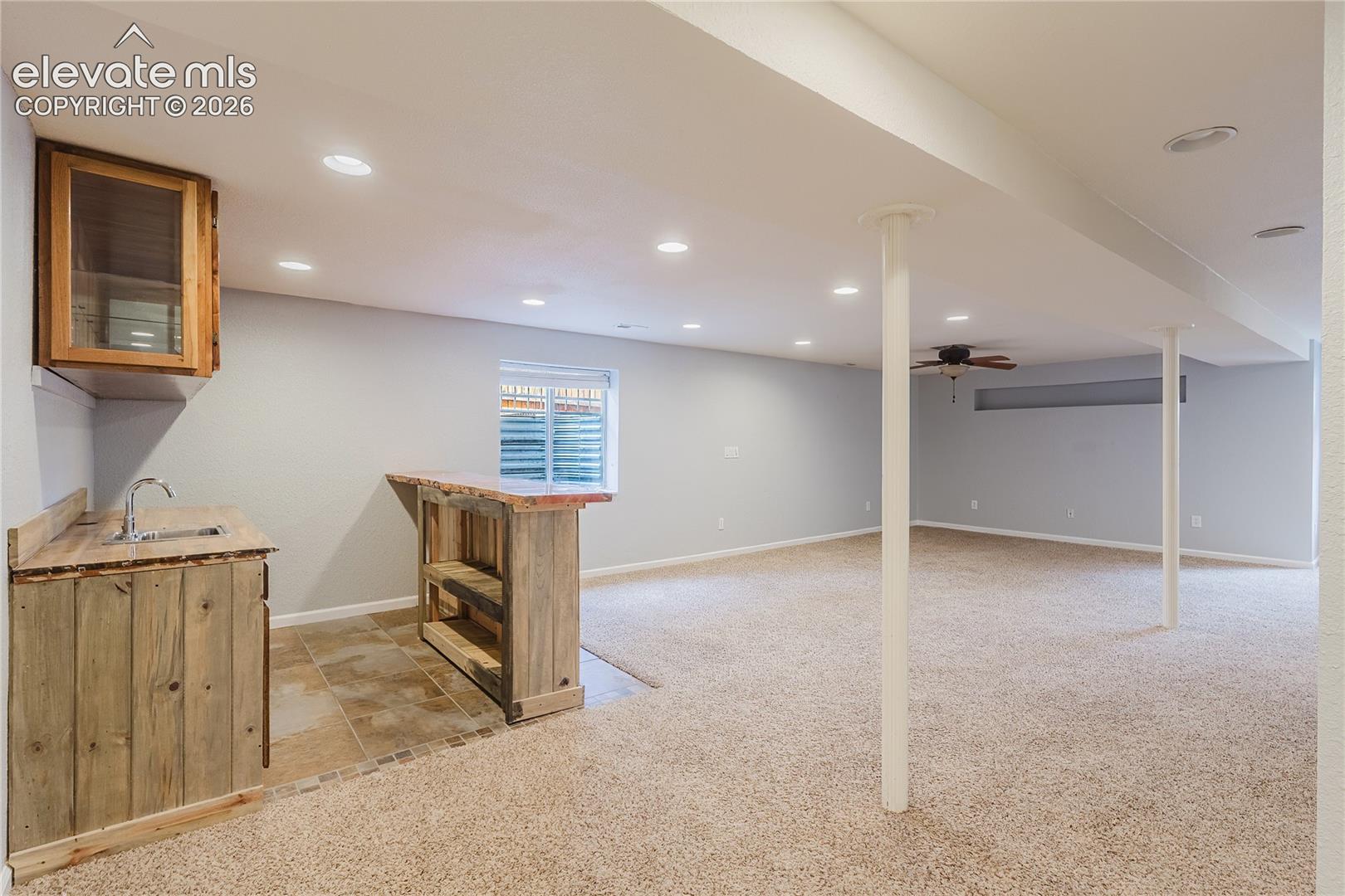 Finished lower level featuring a wet bar with rustic wood-finish cabinetry, tile flooring, recessed lighting, and carpeting