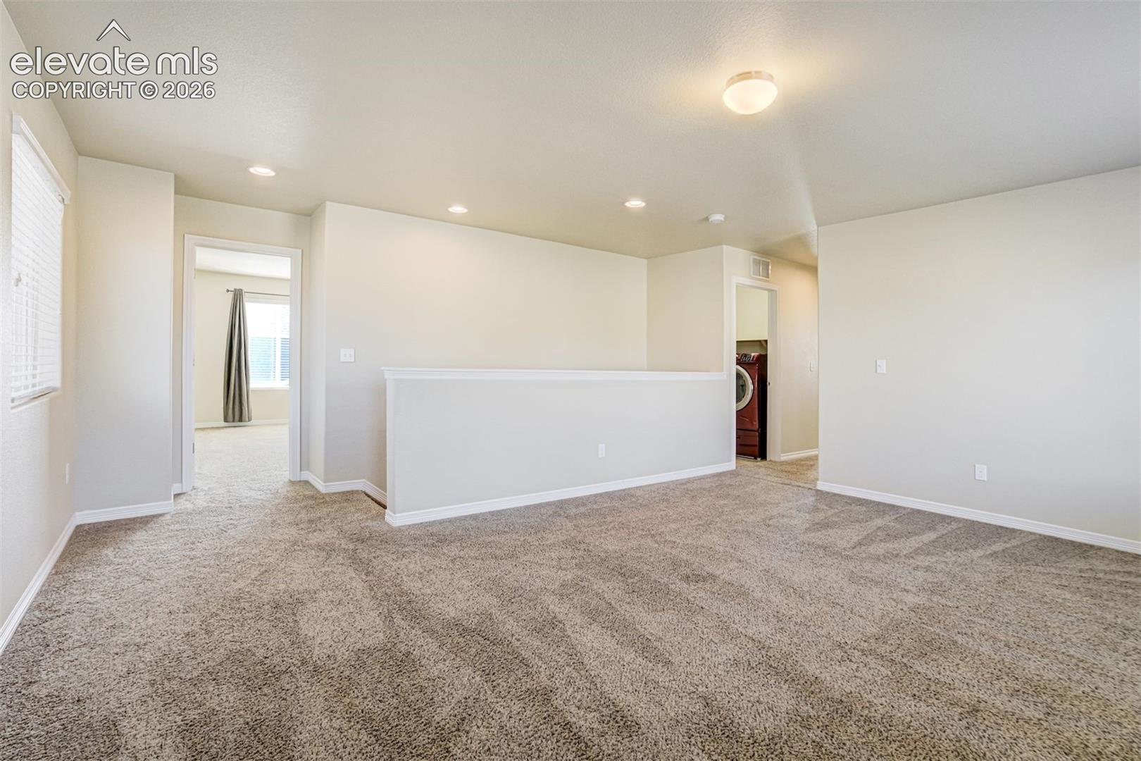 Carpeted loft area with recessed lighting, a window with blinds, and a built-in half-wall
