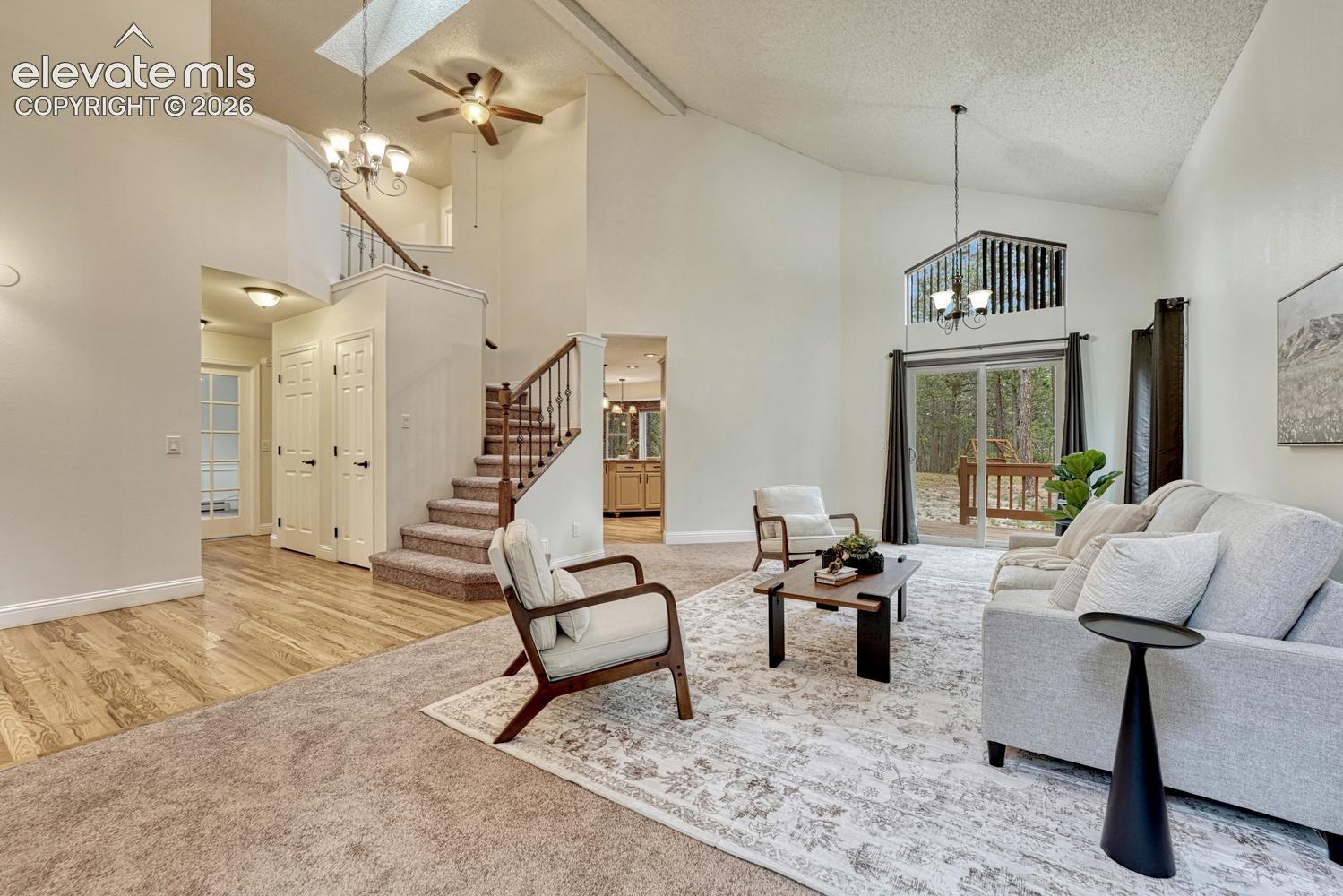 Vaulted ceilings with skylight, wood-finish flooring, staircase with metal balusters, and sliding glass doors with transom window