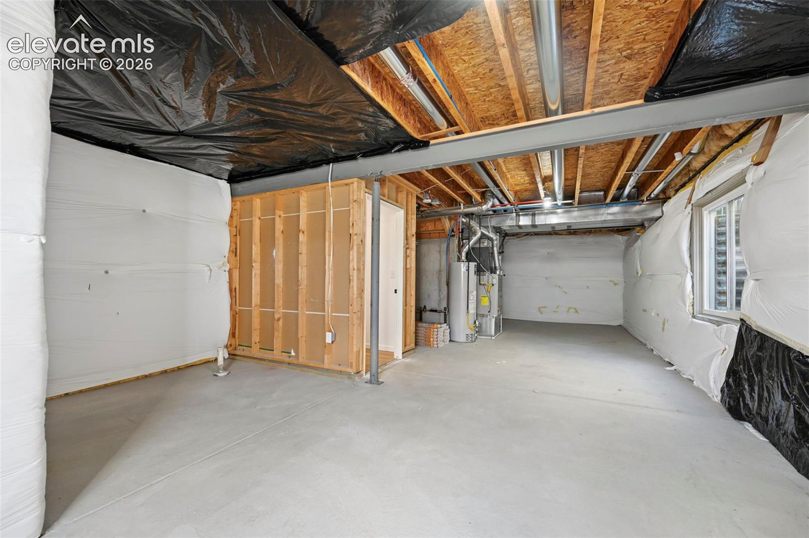Unfinished lower level featuring concrete flooring, exposed wood joists, white vapor barrier wall insulation, a steel support beam, and mechanical systems