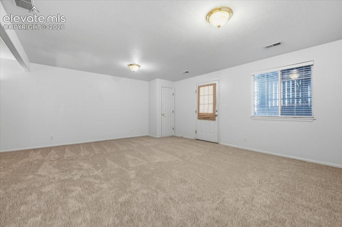 Spacious room featuring neutral carpeting, a white door, a window with blinds, and two flush-mount ceiling lights