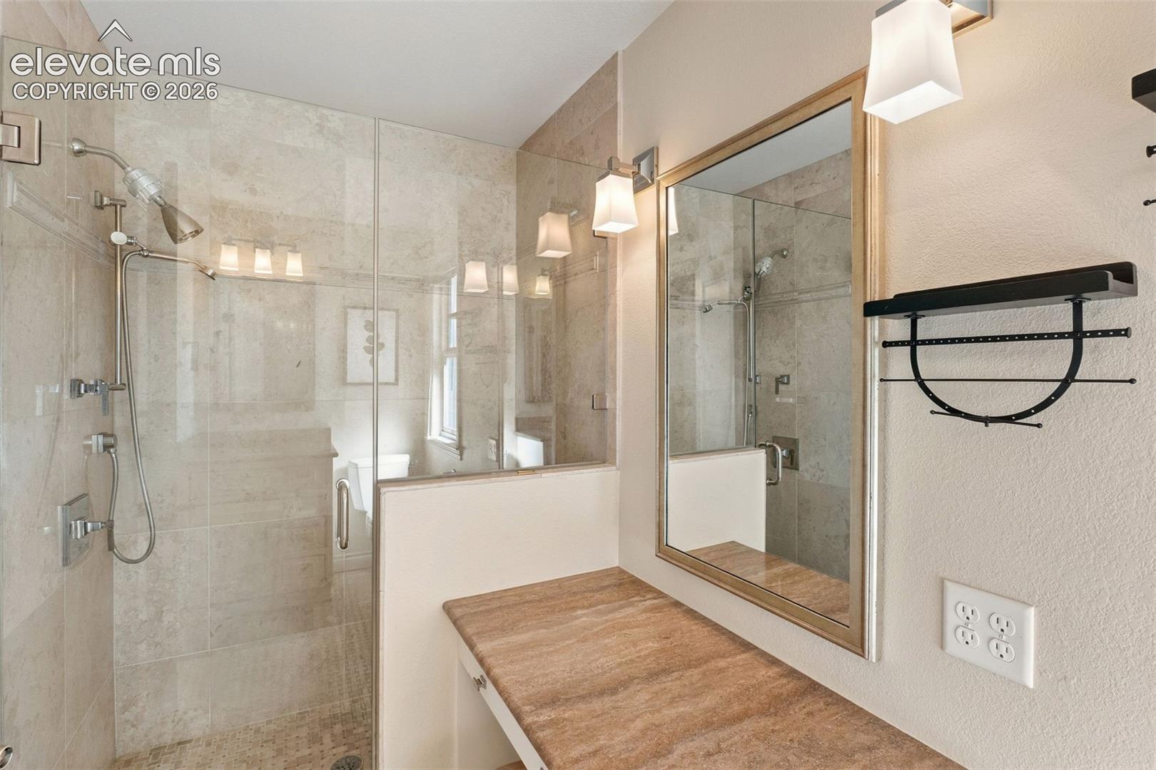 Walk-in shower with floor-to-ceiling stone tile, glass enclosure, polished metal fixtures, built-in vanity with stone countertop, and wall-mounted lighting