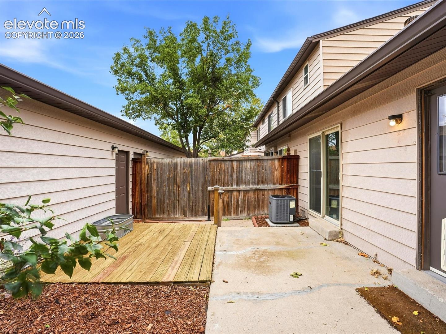 Exterior space featuring horizontal siding, a wood-decked patio, a concrete patio area, and enclosed wood fencing