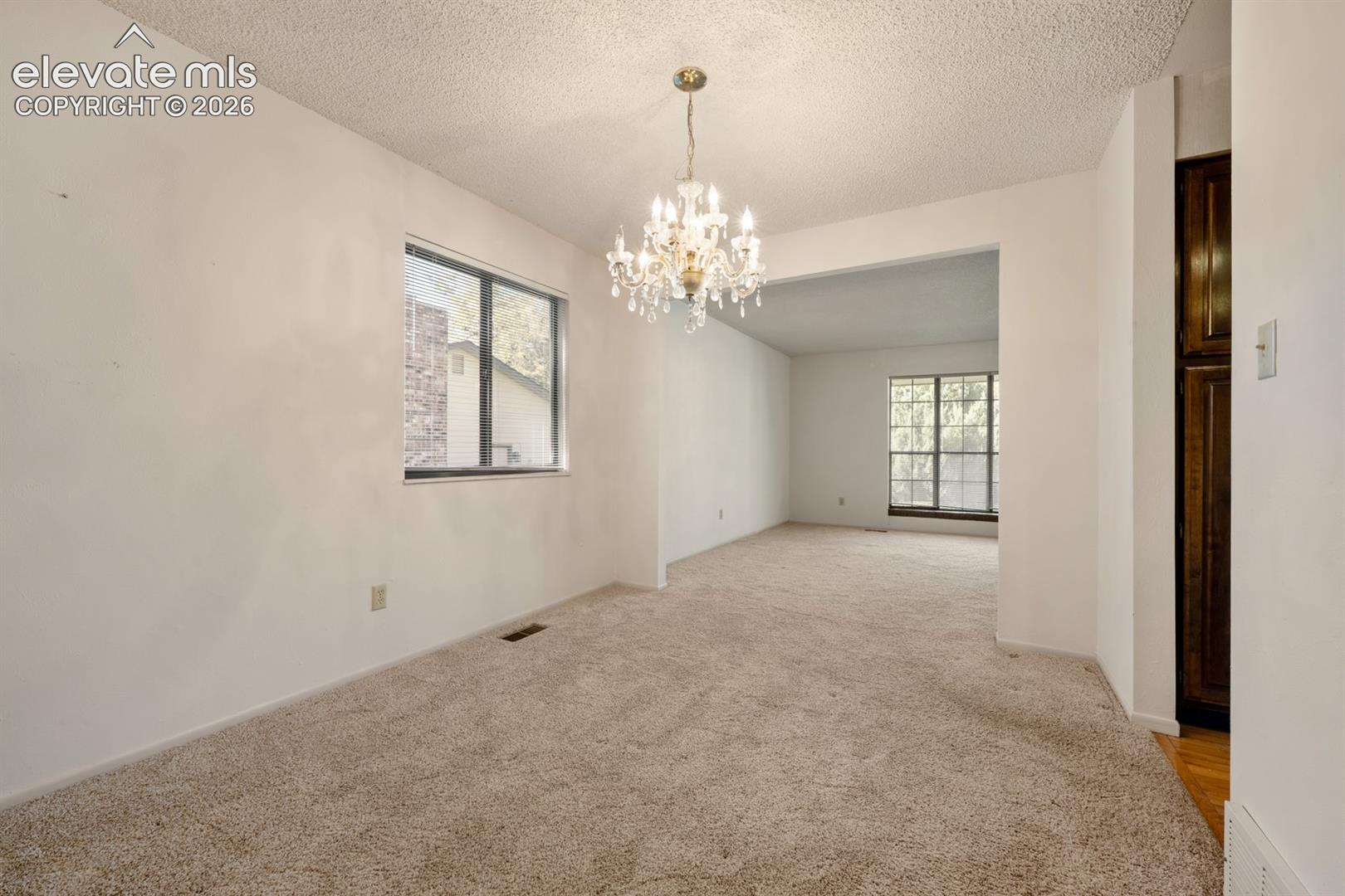 Dining area featuring neutral wall-to-wall carpeting, an ornate multi-arm crystal chandelier, and large windows with grid muntins
