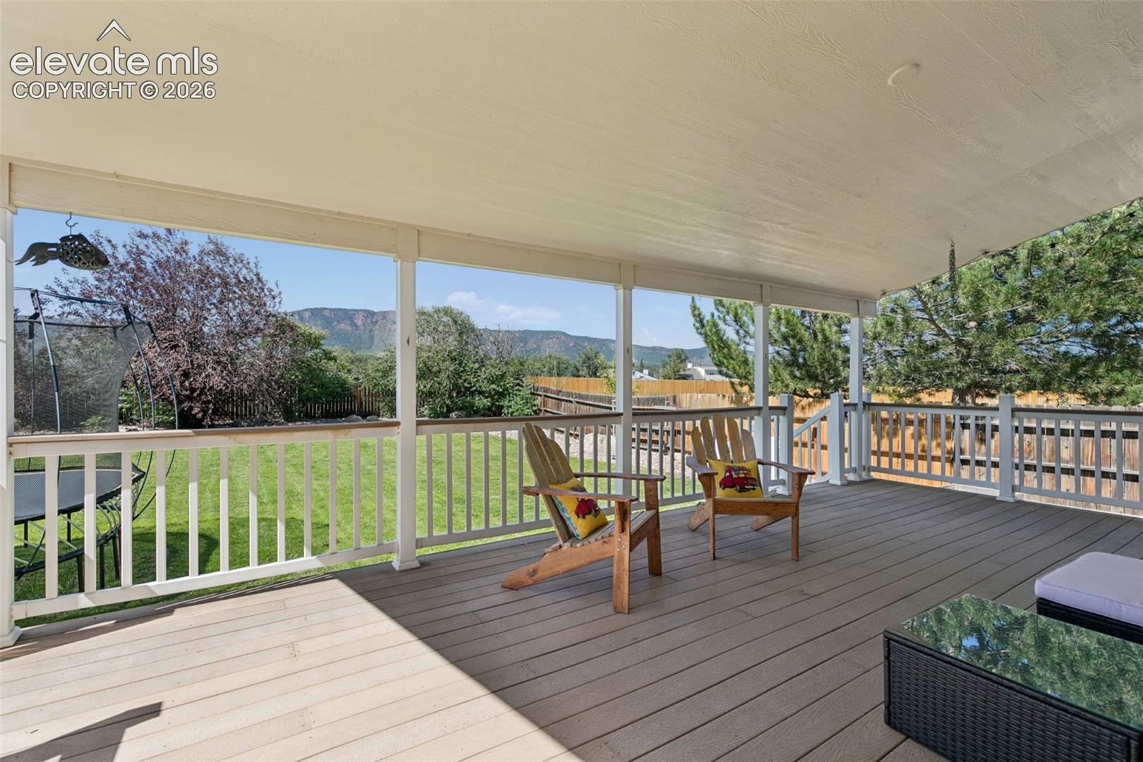 Covered patio featuring composite decking, white railing, and a mountain backdrop