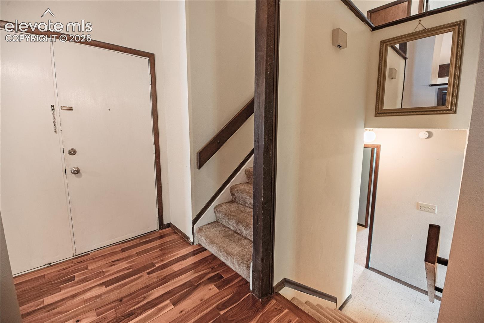 Foyer featuring wood-finish flooring, carpeted stairs with a wooden handrail, and a vertical structural wood beam