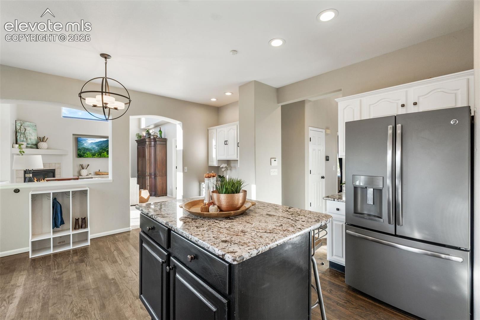 Kitchen featuring a central island with stone countertop, stainless steel refrigerator, white cabinetry, wood-finish flooring, and a spherical chandelier