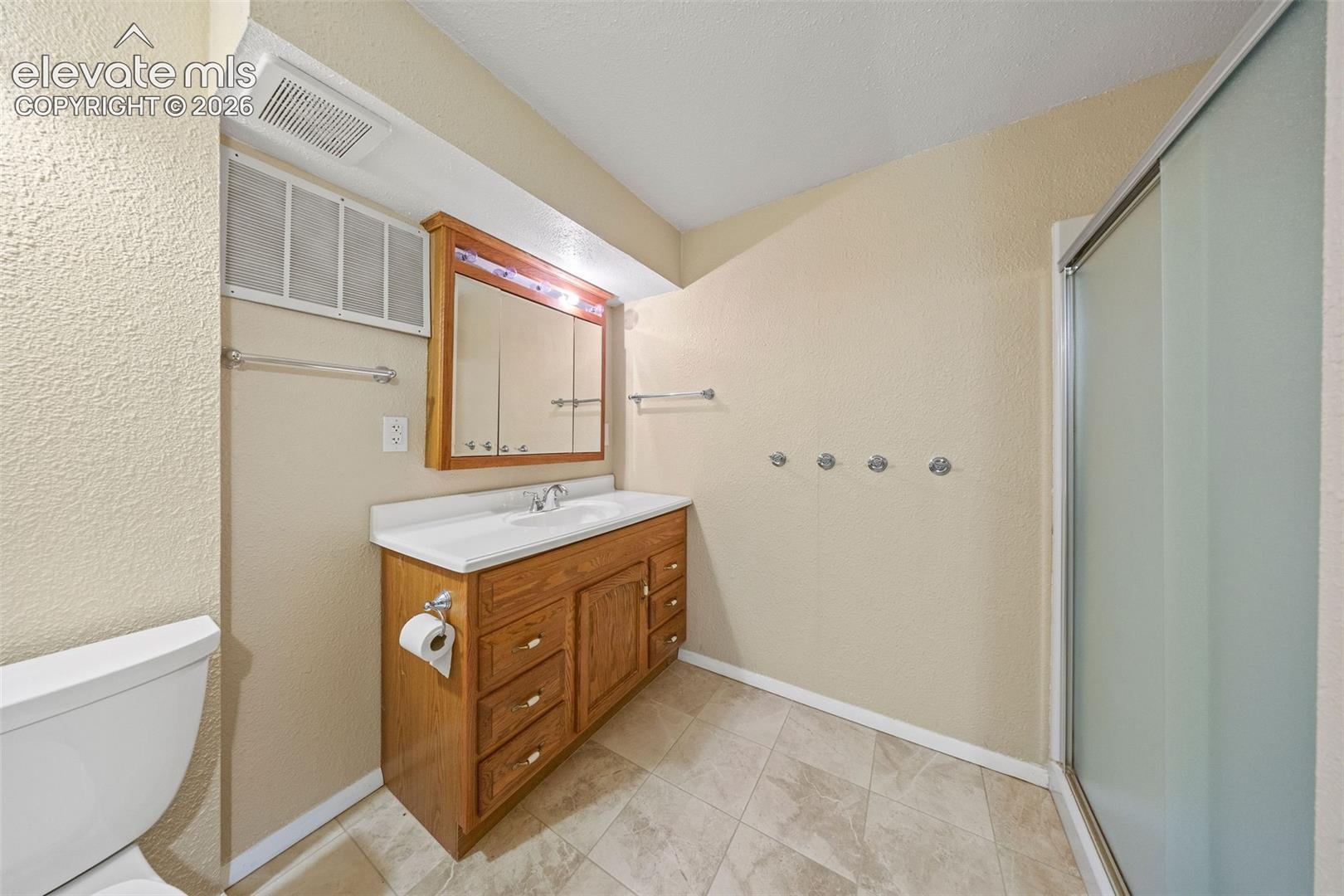 Bathroom featuring a wood vanity with integrated basin and countertop, illuminated medicine cabinet, stall shower with sliding glass doors, and tile flooring