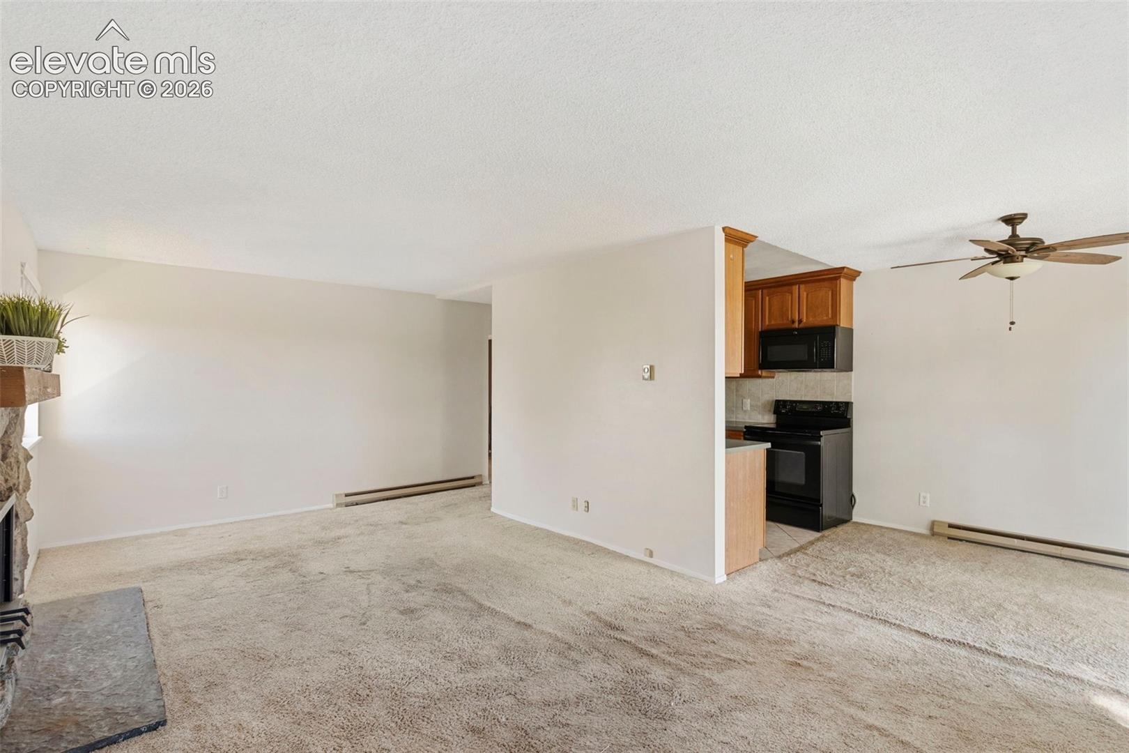 Living area featuring a stone fireplace with hearth, a ceiling fan, and carpet flooring