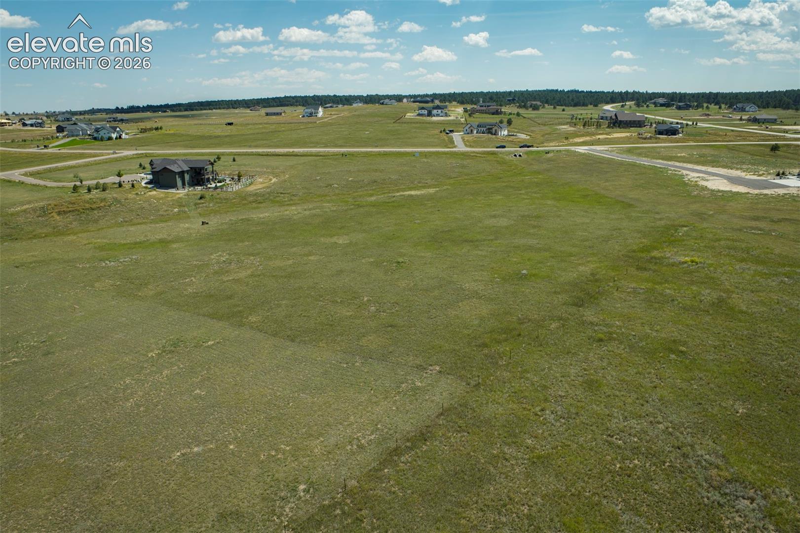 Expansive undeveloped lot featuring natural vegetation, surrounded by distant residential properties