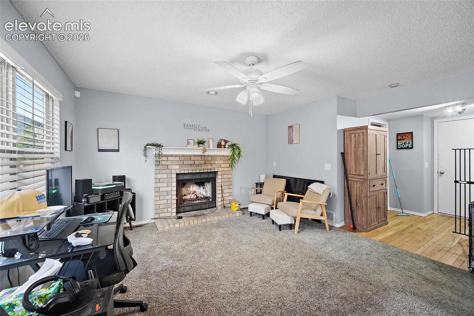 Brick fireplace with a white mantel, ceiling fan with integrated lighting, and wood-finish flooring