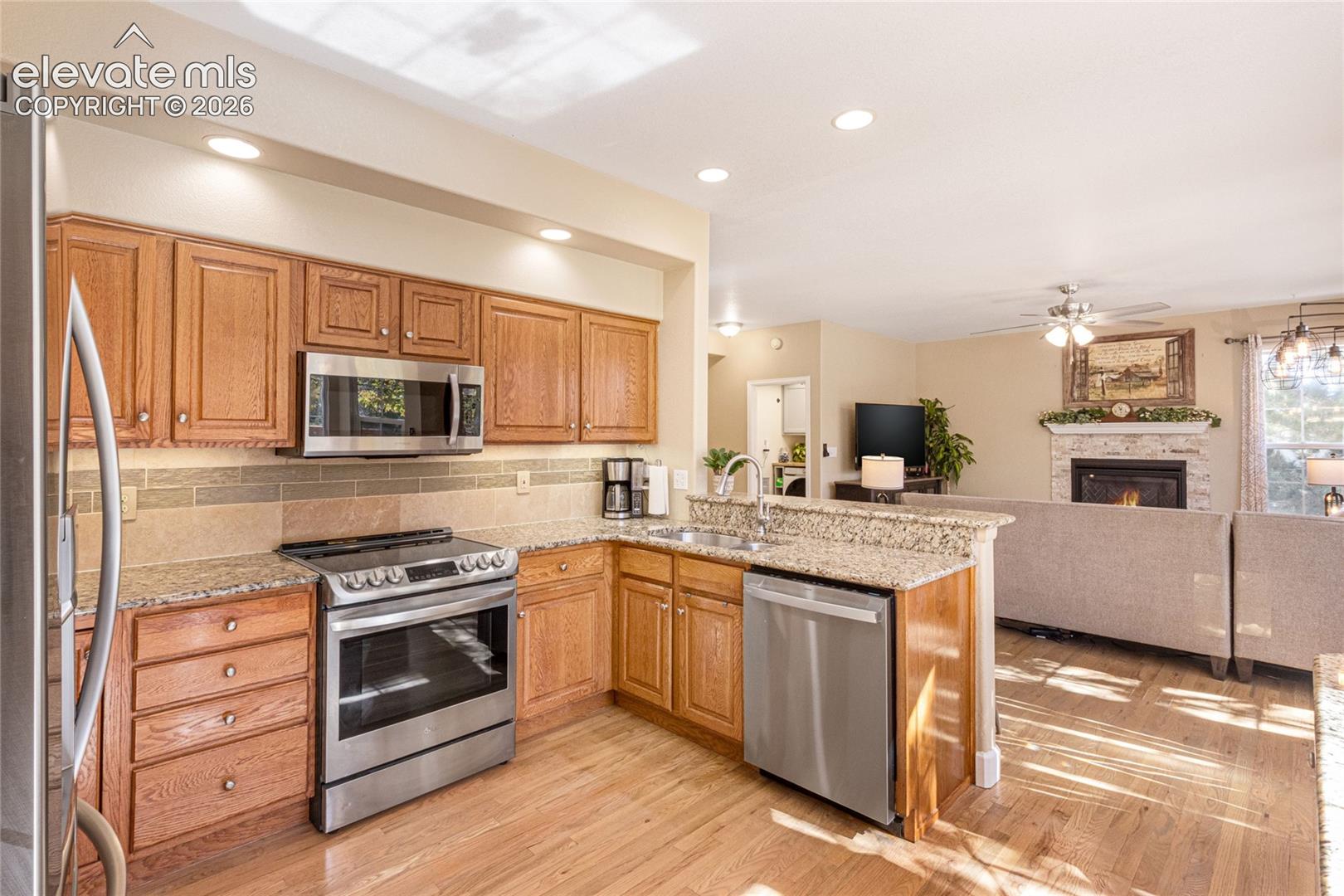 Kitchen featuring wood cabinetry, stone-finish countertops, stainless steel appliances, and a stacked-stone fireplace surround