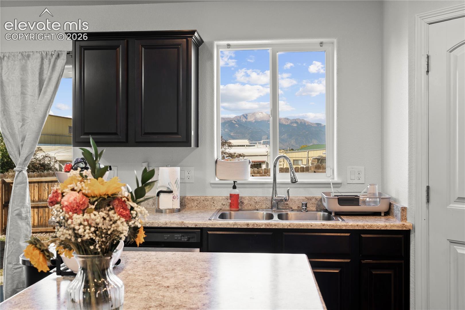 Dark-finish shaker-style cabinetry, stone-texture laminate countertops, double-basin stainless steel sink with pull-down faucet, and mountain backdrop