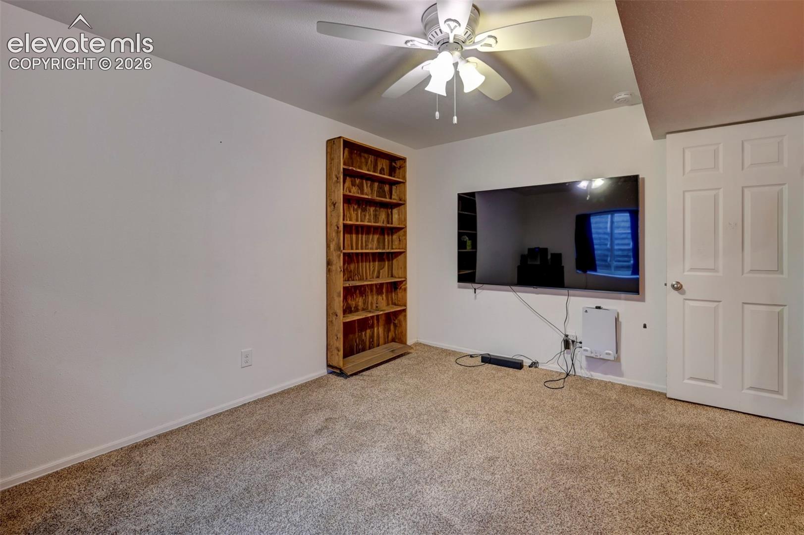 Recessed wall-mounted television, built-in wooden shelving, and ceiling fan with integrated lighting