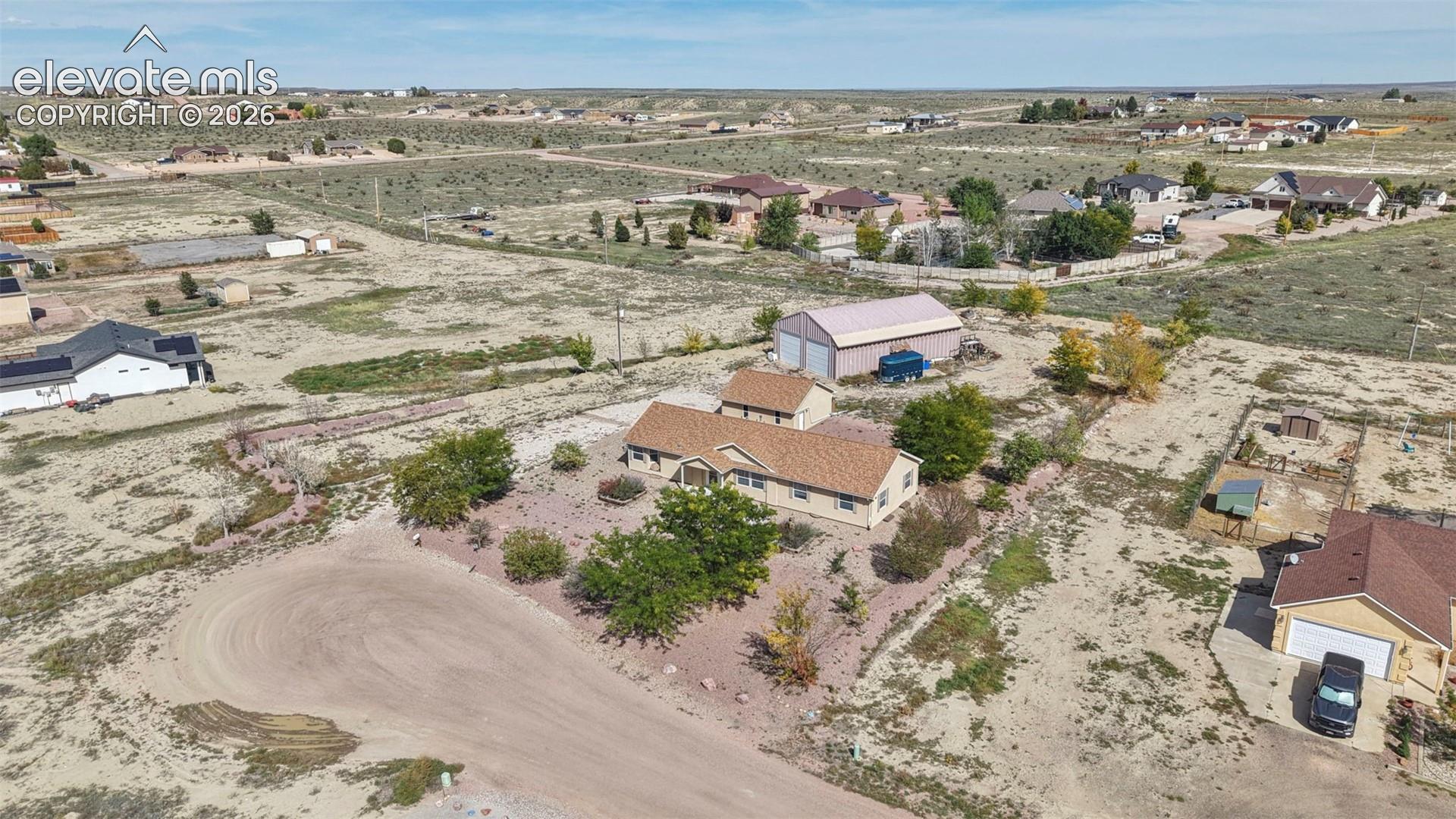 Aerial perspective of a detached residential property featuring a shingled roof, an expansive lot, a detached metal-sided outbuilding, and mature trees