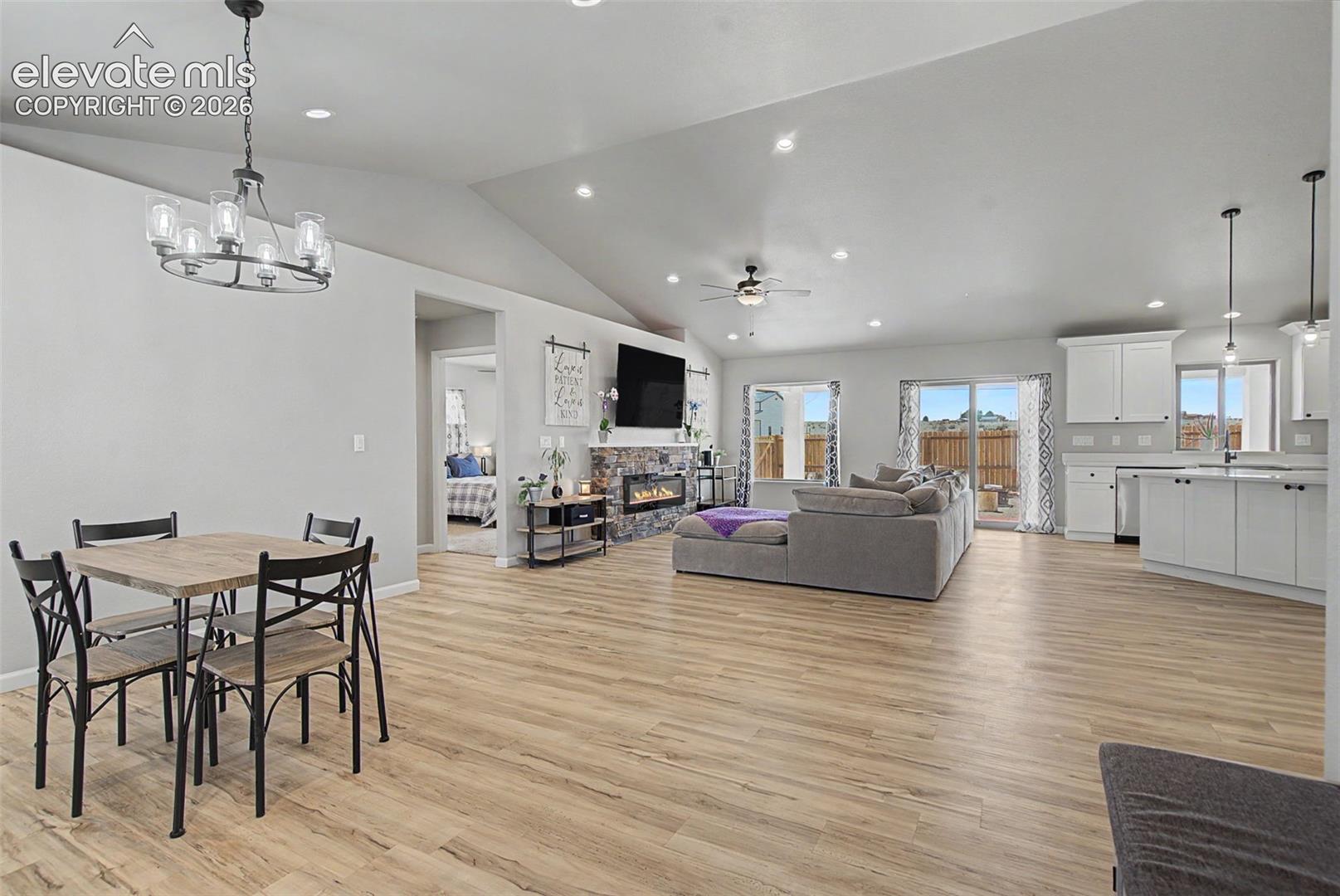 Open-concept living space featuring wood-finish flooring, vaulted ceilings, recessed lighting, a stone-clad fireplace, and sliding glass doors