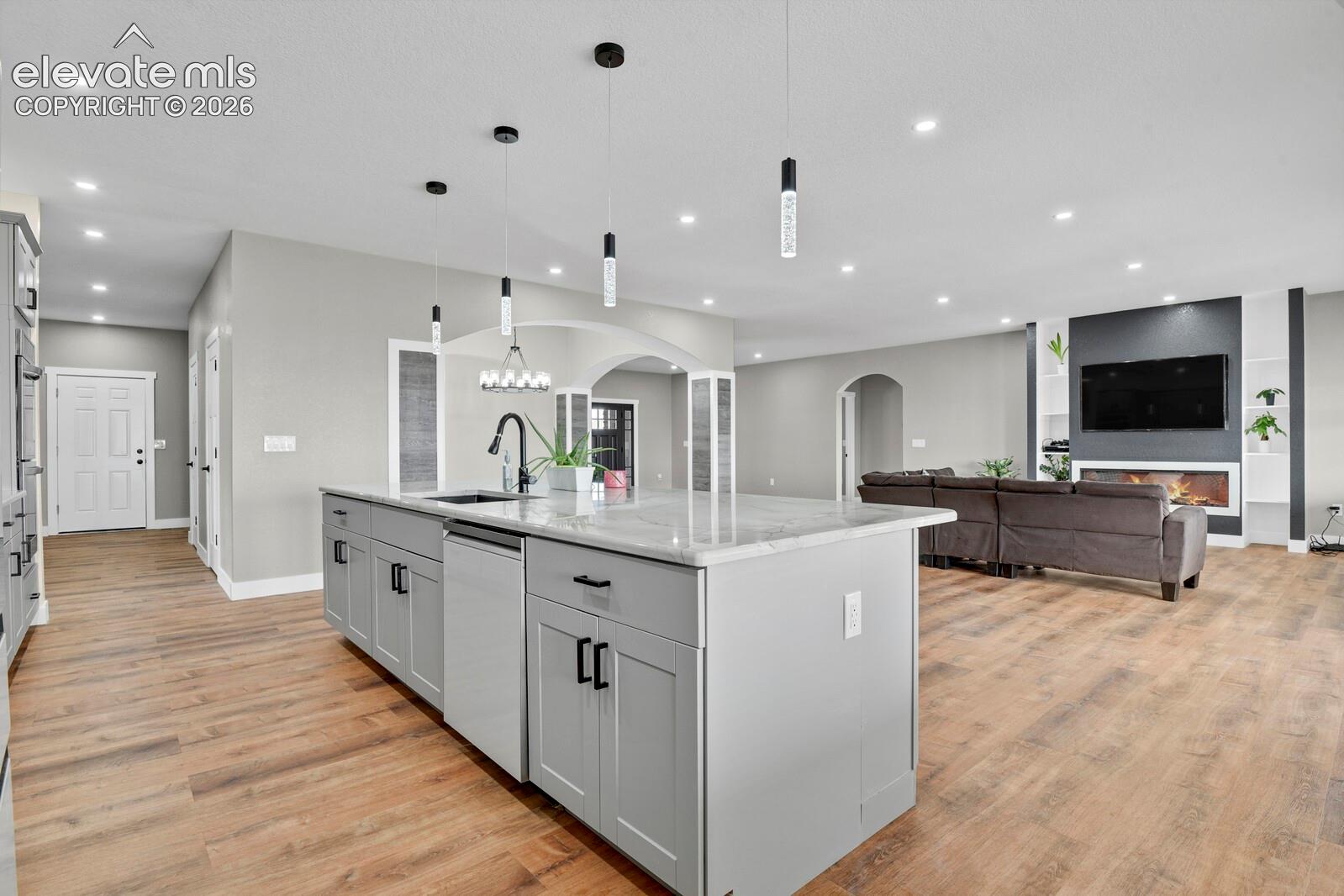 Kitchen island with stone countertop and matte black hardware, recessed lighting, pendant fixtures, wood-finish flooring, and built-in fireplace with flanking shelving