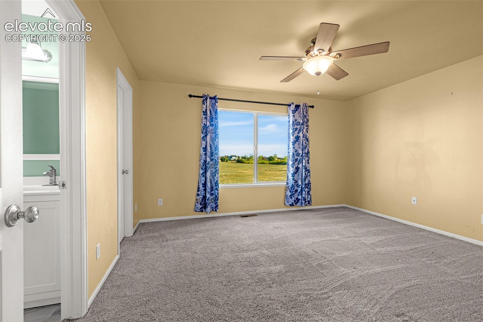 Neutral-toned bedroom featuring carpeting, a central ceiling fan with integrated lighting, and a single-pane window
