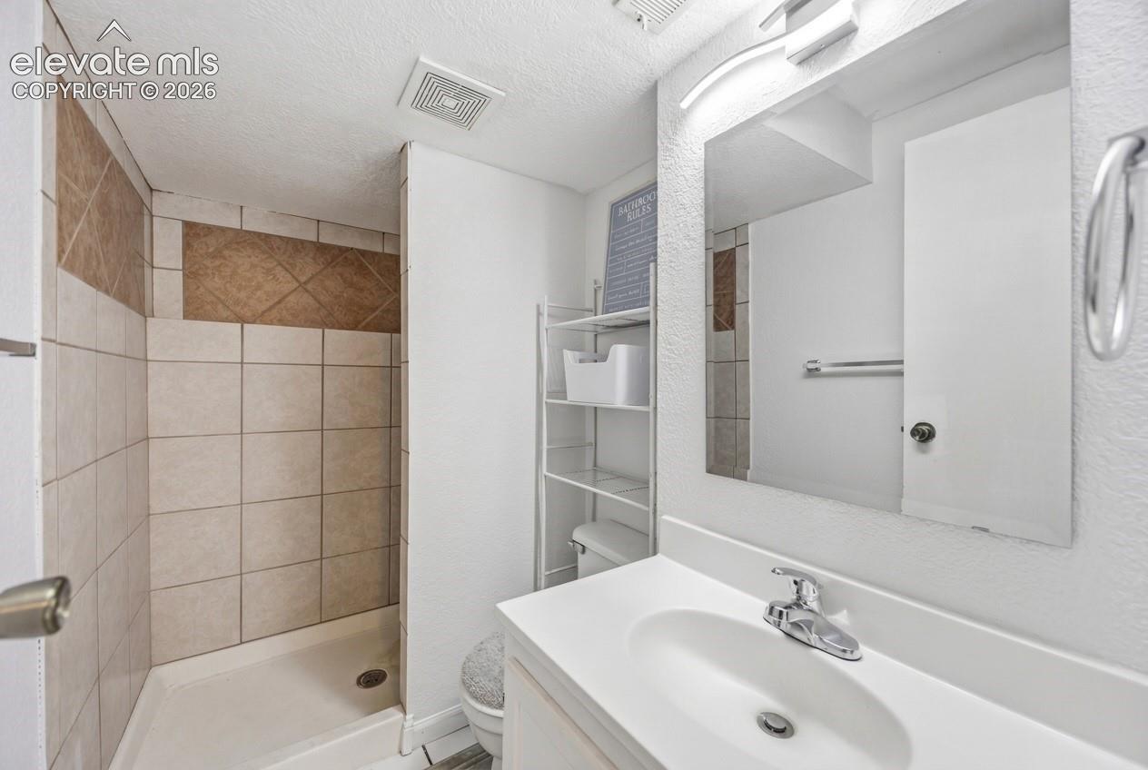 Shower stall with tiled walls, vanity with integrated sink, chrome faucet, and mirrored medicine cabinet