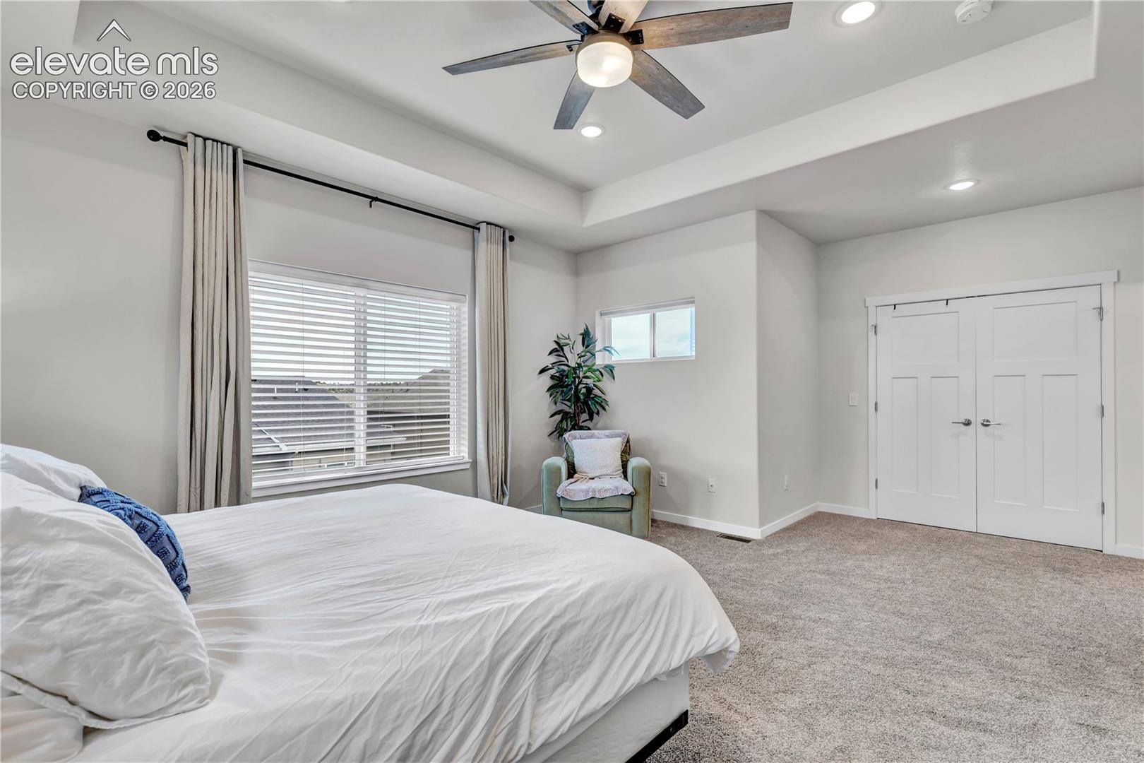Tray ceiling with recessed lighting, ceiling fan with integrated light, dual pane window, additional transom window, and paneled double doors