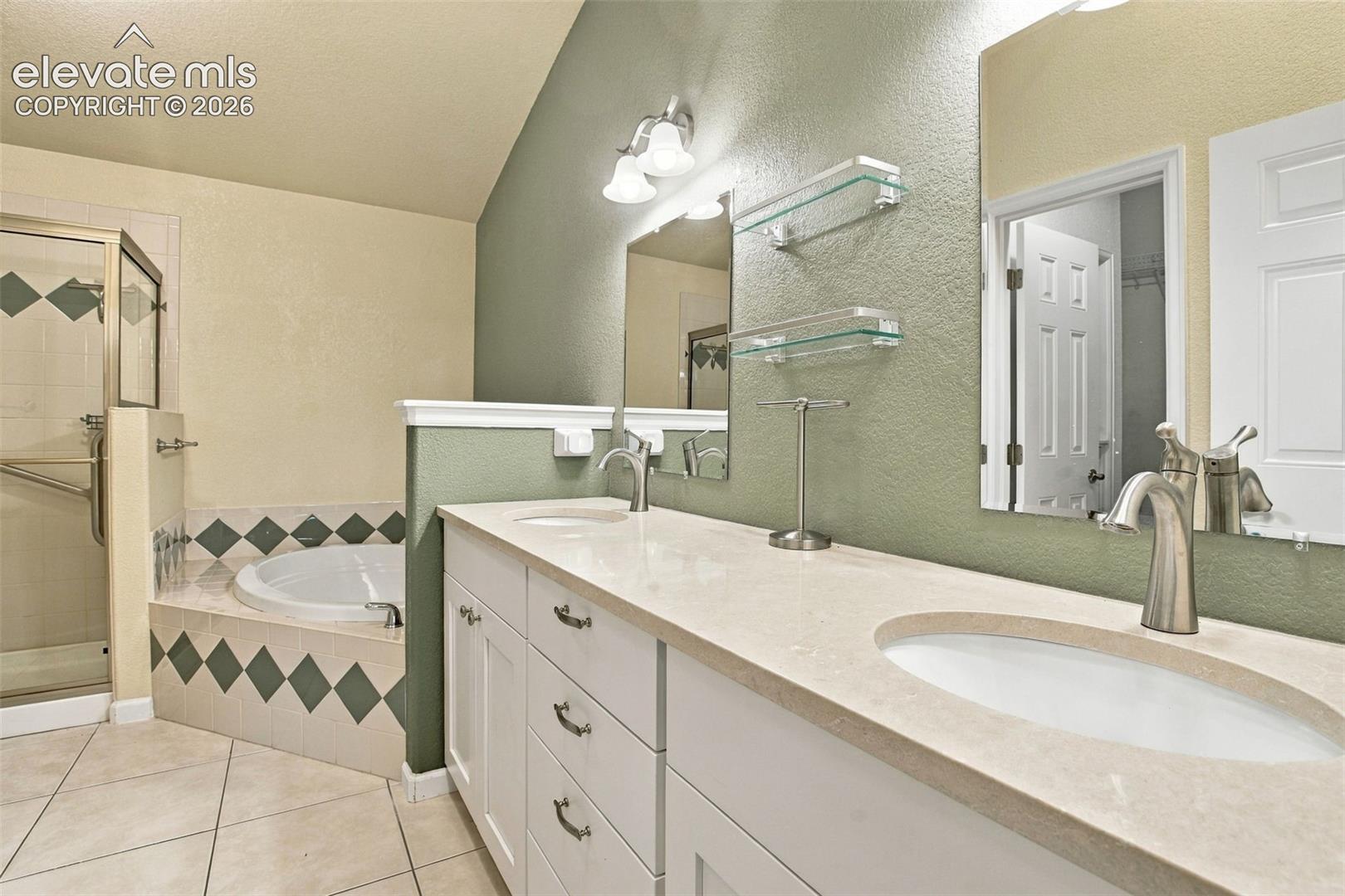Dual vanity with solid surface countertops, under-mount sinks, built-in cabinetry, corner soaking tub with tile surround, and enclosed glass shower