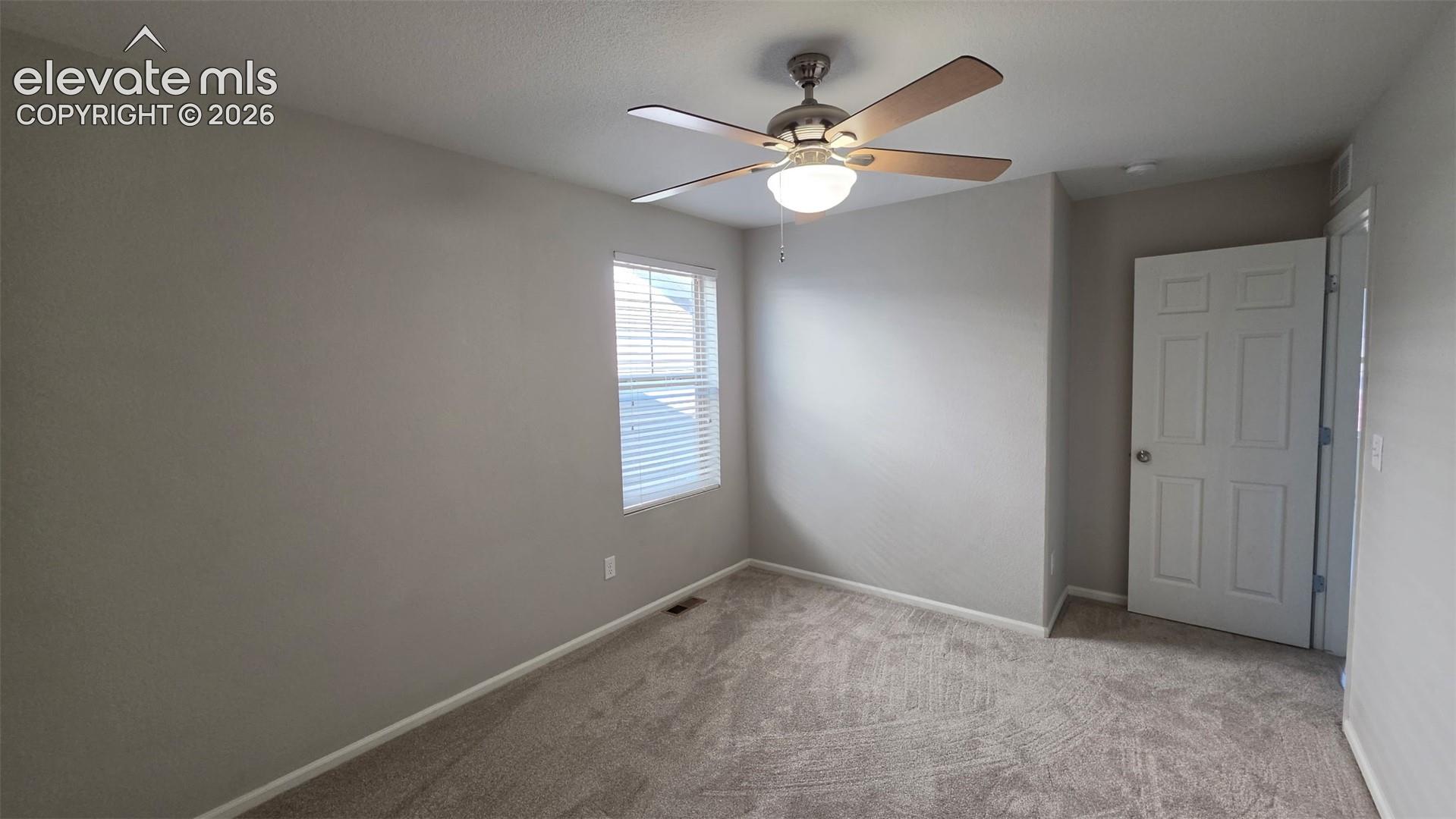 Neutral interior featuring carpeted flooring, a ceiling fan with integrated lighting, a single window, and a six-panel door