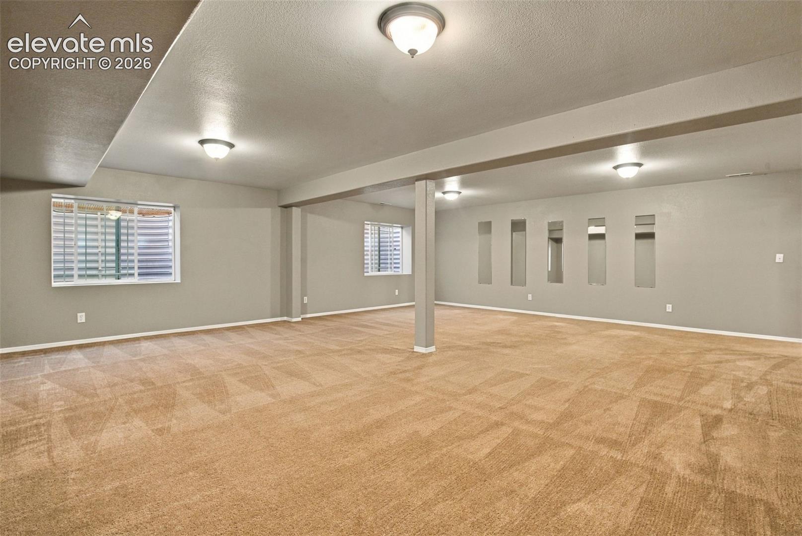Spacious room featuring carpeting, recessed wall niches, multiple windows with blinds, and flush mount ceiling lighting
