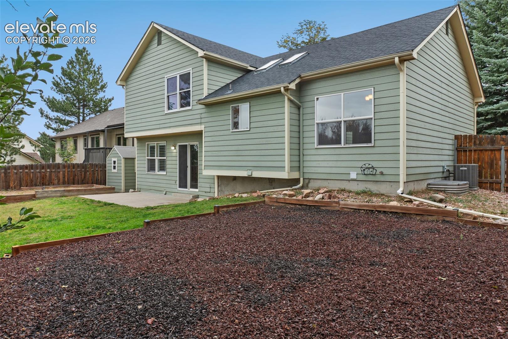 Horizontal siding exterior with multiple windows, concrete patio, and a shed, all surrounded by a wood fence