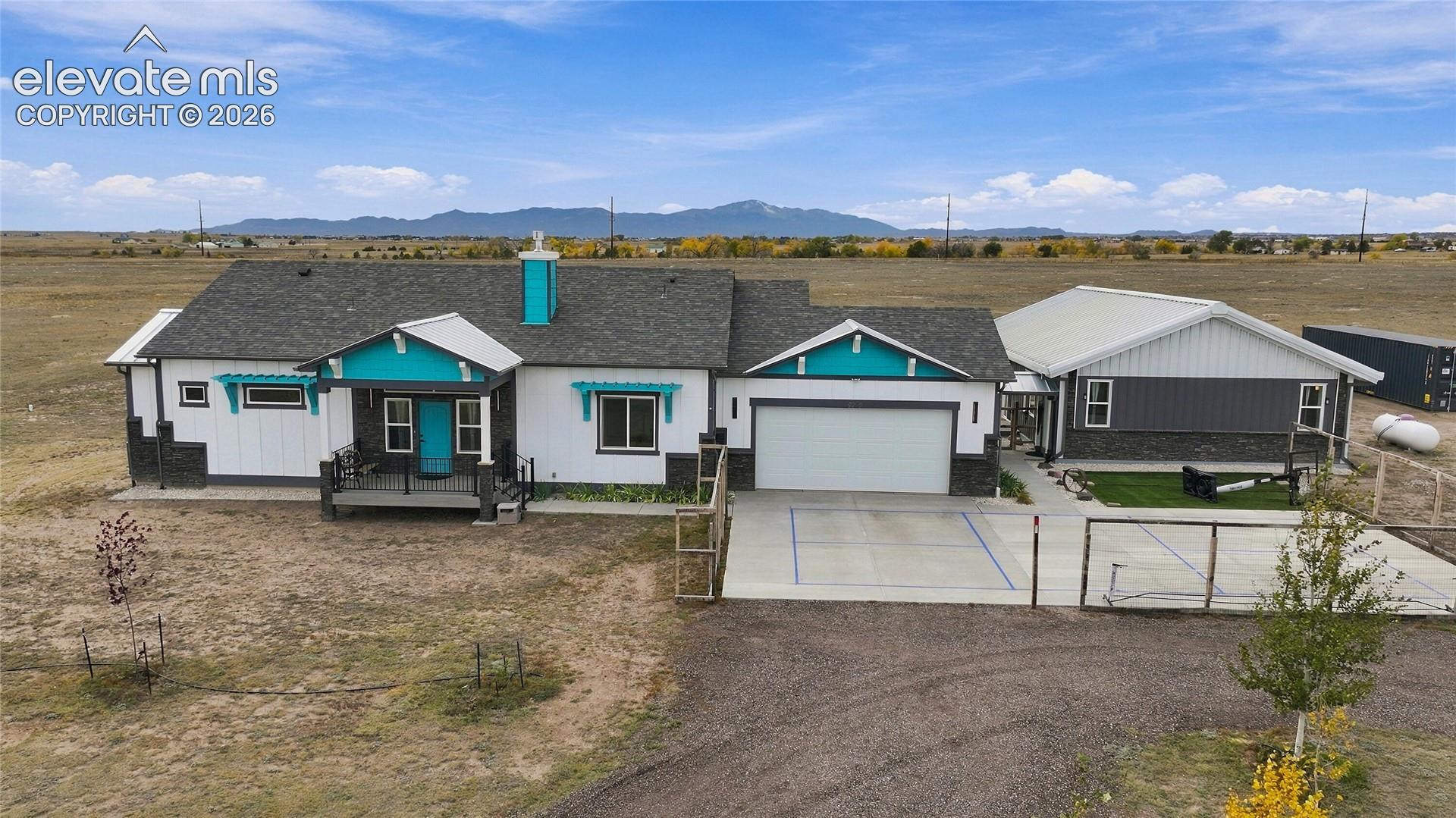 Single-story exterior featuring white vertical siding, stone veneer base, covered front porch, attached multi-car garage, and mountain backdrop