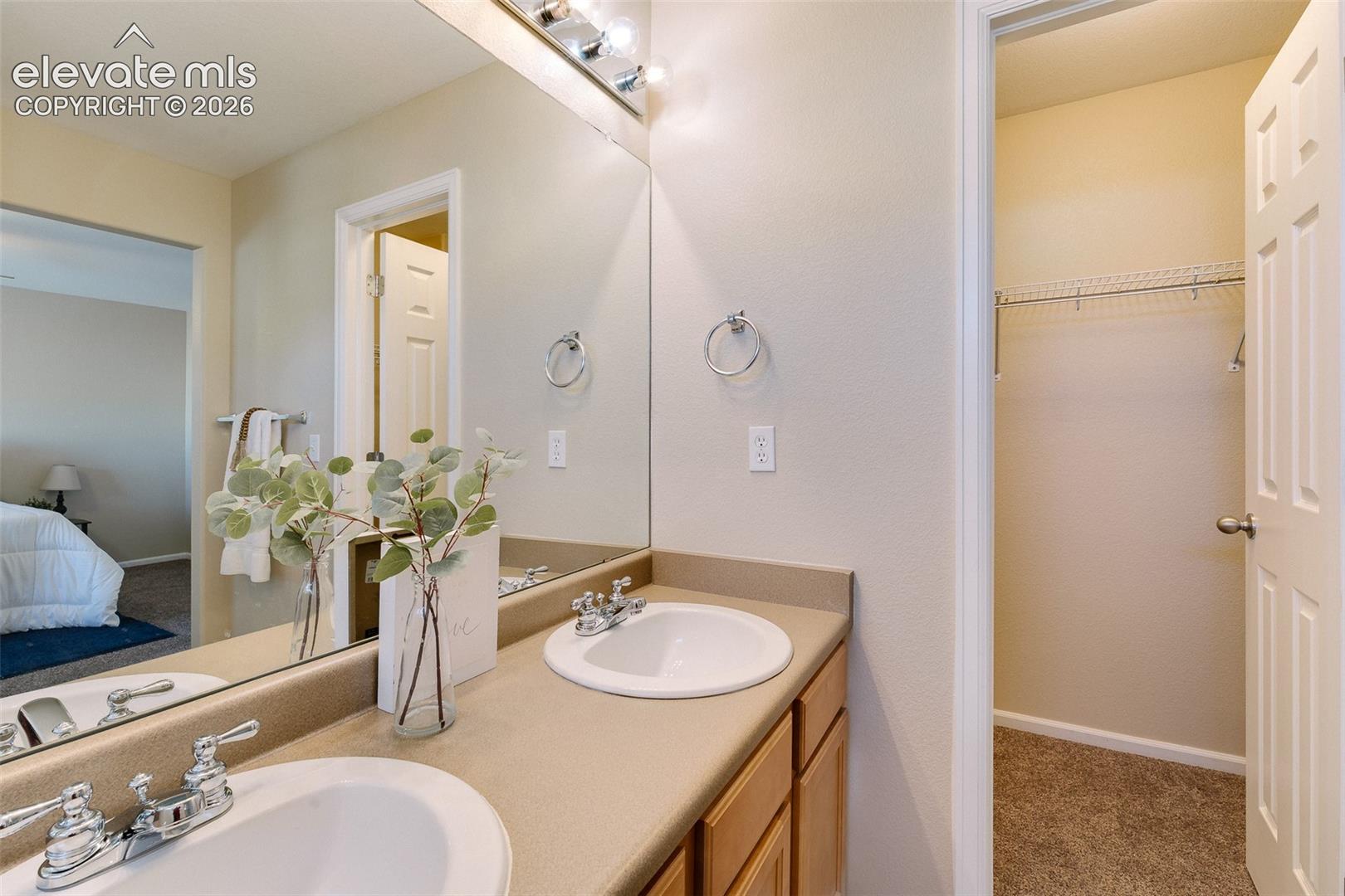 Vanity featuring dual white drop-in sinks, an expansive wall-to-wall mirror, and neutral-toned countertops