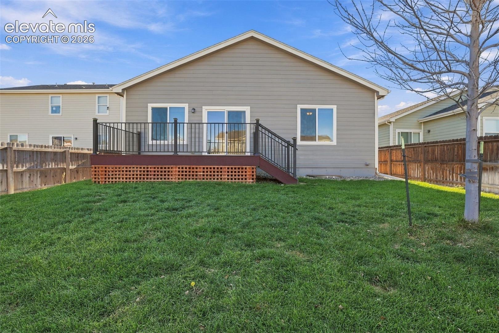 Rear exterior featuring horizontal lap siding, an elevated wood deck with black metal railing, and a fenced backyard