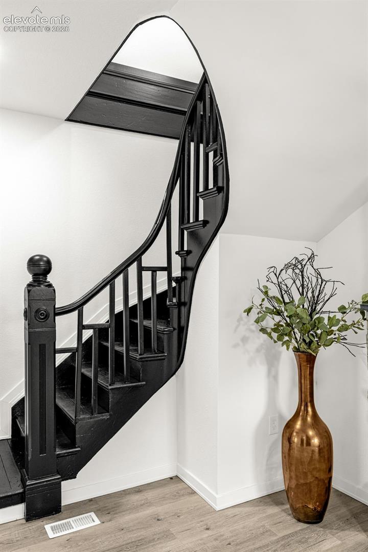 Curved black staircase featuring a substantial newel post, balusters, and handrail, complemented by light wood-finish flooring and white baseboards