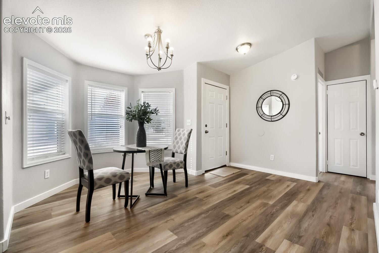 Bay window featuring three paneled windows, wood-finish flooring, and a multi-arm chandelier