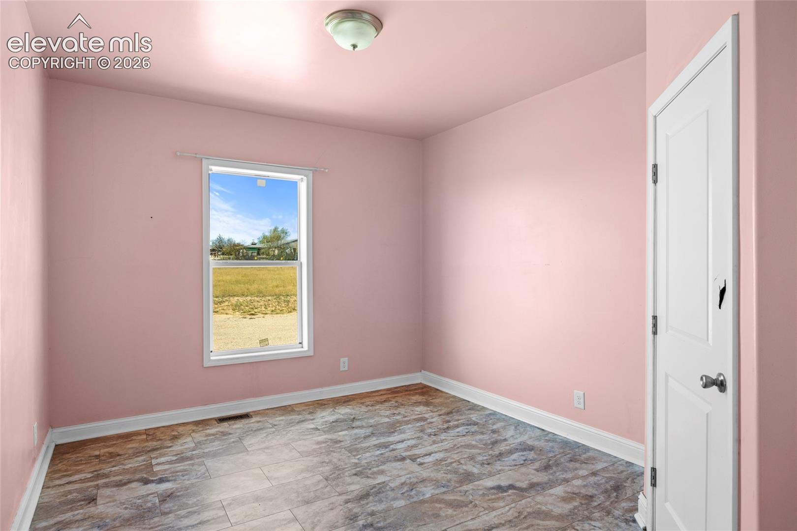 Interior room featuring wood-finish tile flooring, a single-hung window with exterior landscape exposure, and a flush-mount ceiling light fixture