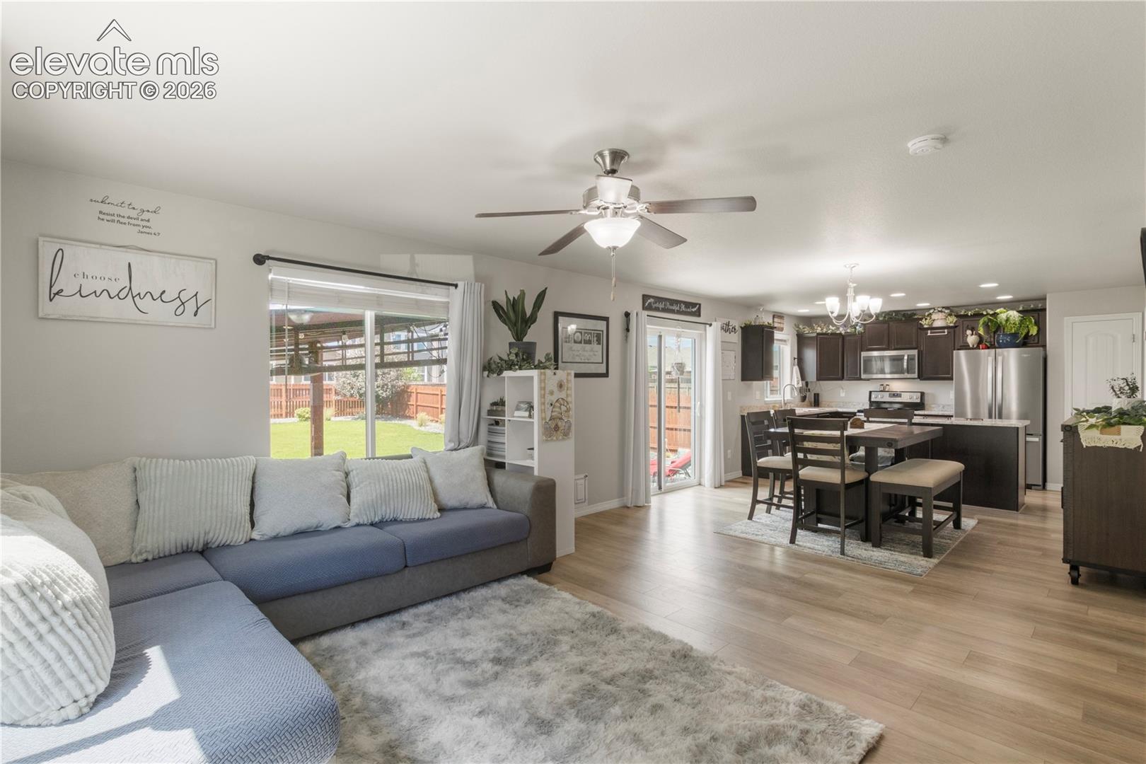 Open-concept living space featuring wood-finish flooring, a ceiling fan with integrated lighting, and sliding glass doors to the exterior
